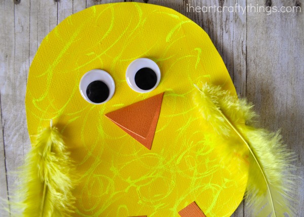 Close up image of where to glue the googly eyes, folded beak and yellow feathers on the chick craft.